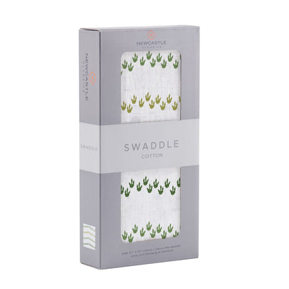 Angled front view of the packaged Dino Feet baby swaddle blanket folded inside a grey Newcastle Classics window display box.