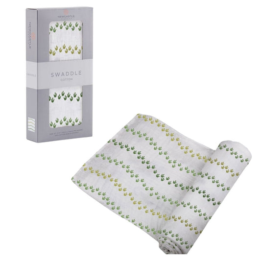 Partially unrolled Newcastle Classics Dino Feet cotton muslin swaddle blanket displayed next to its grey window packaging box.