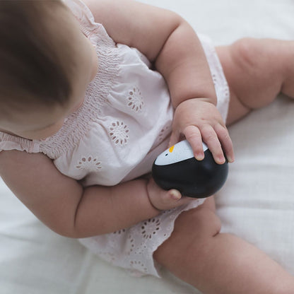 A baby sitting in a white onesie holding the smooth, rounded PlanToys wooden penguin wobbler.