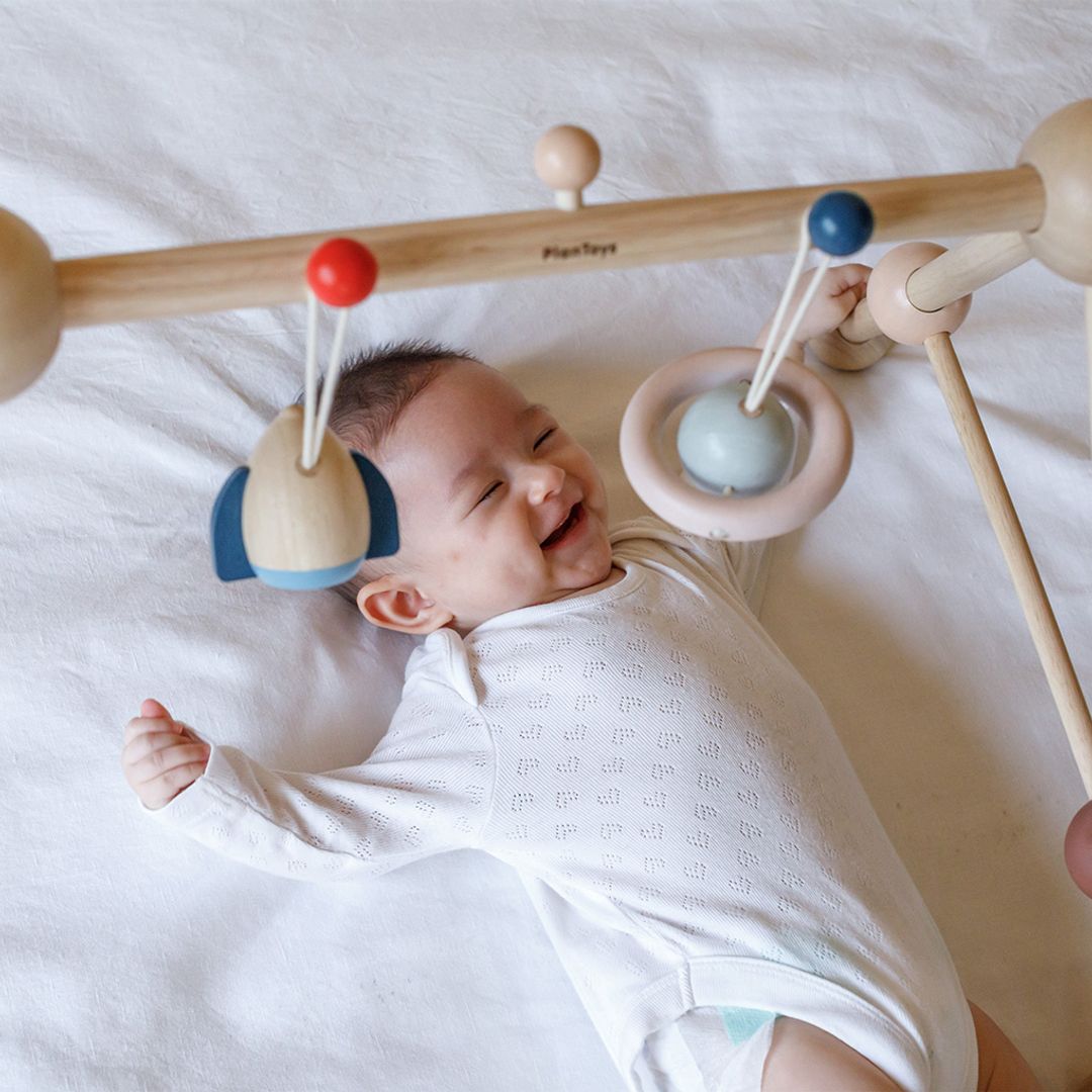 A close-up of a baby happily engaging with the dangling sensory toys on the PlanToys play gym.