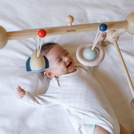 A close-up of a baby happily engaging with the dangling sensory toys on the PlanToys play gym.