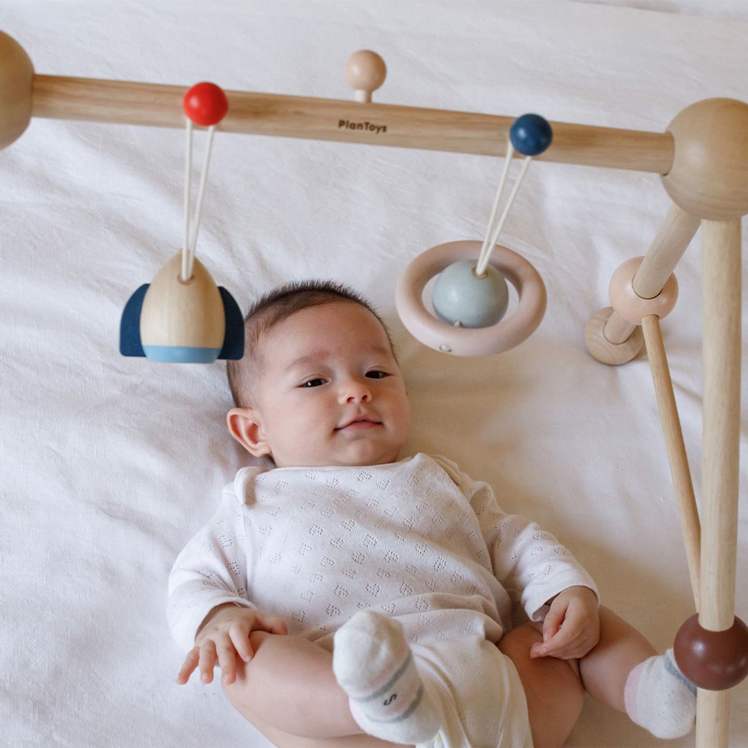 An infant developing hand-eye coordination by reaching for the eco-friendly PlanToys wooden rocket toy.
