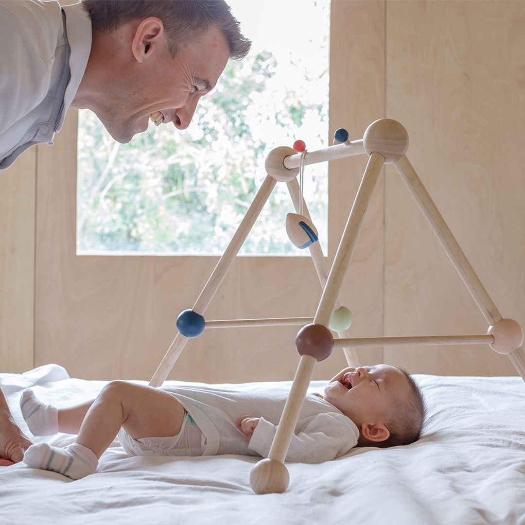 A bonding moment between parent and baby as they play together under the PlanToys wooden activity center.