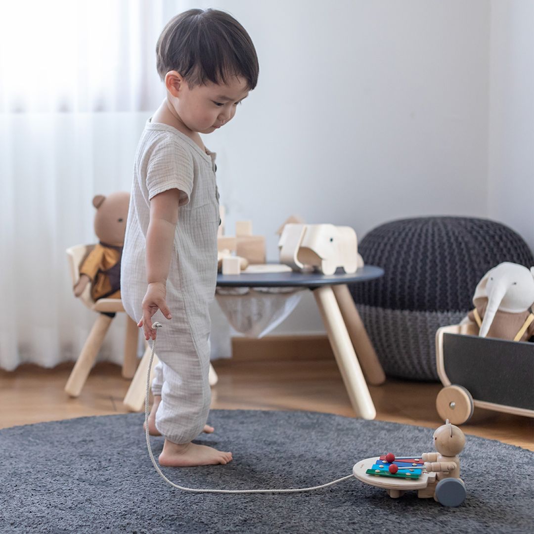 A young boy in a neutral outfit holding the pull string of his eco-friendly PlanToys xylophone bear.