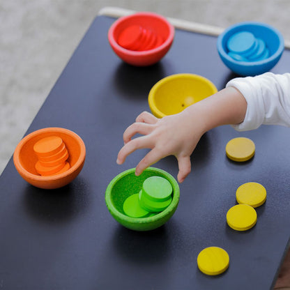 Close-up of a child's hand placing a green wooden coin into the matching eco-friendly PlanToys sorting cup.