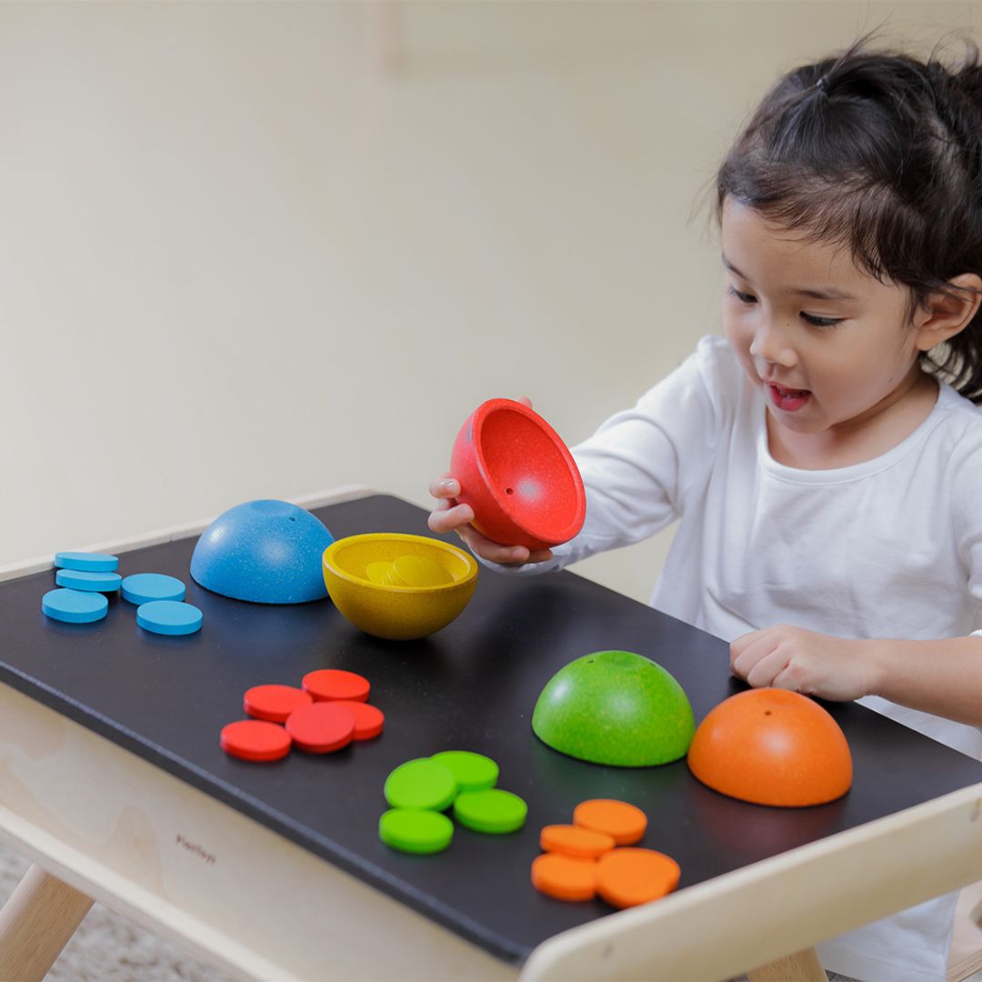 A toddler engaging in open-ended play by turning the PlanToys wooden sorting cups upside down to hide the colorful coins.