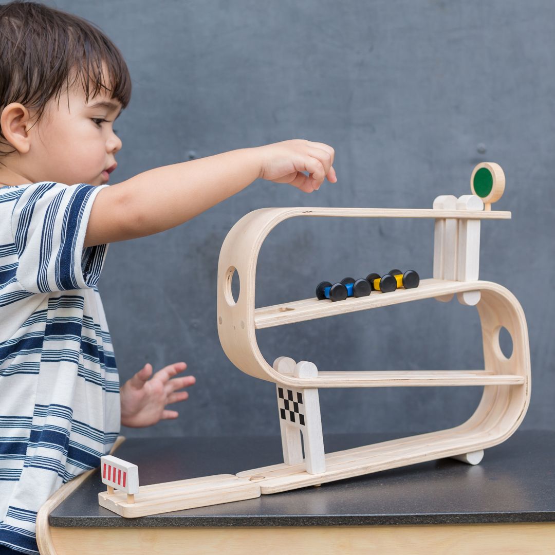 A toddler dropping a toy car into the top level of the PlanToys sustainable wooden ramp racer.