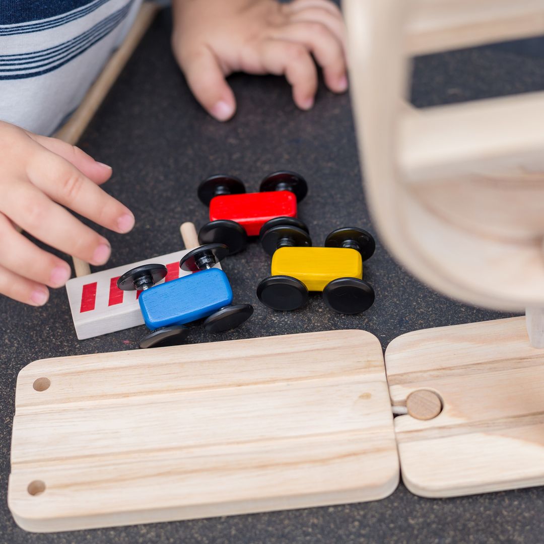 Close-up of the three colorful wooden cars reaching the finish line barrier on the PlanToys racing track.