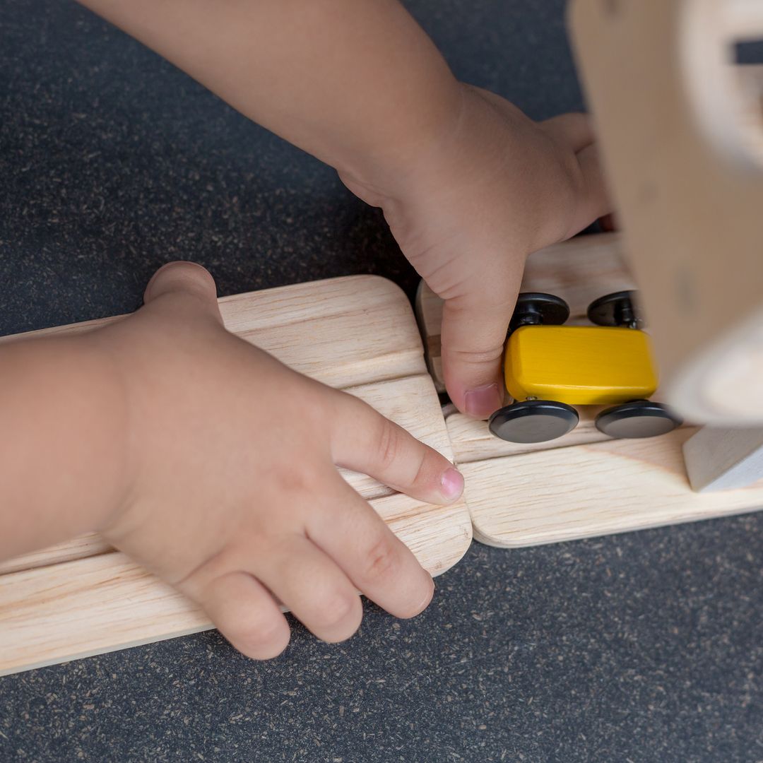 A child's hands connecting the bottom ramp of the PlanToys racer directly to an eco-friendly wooden track piece.