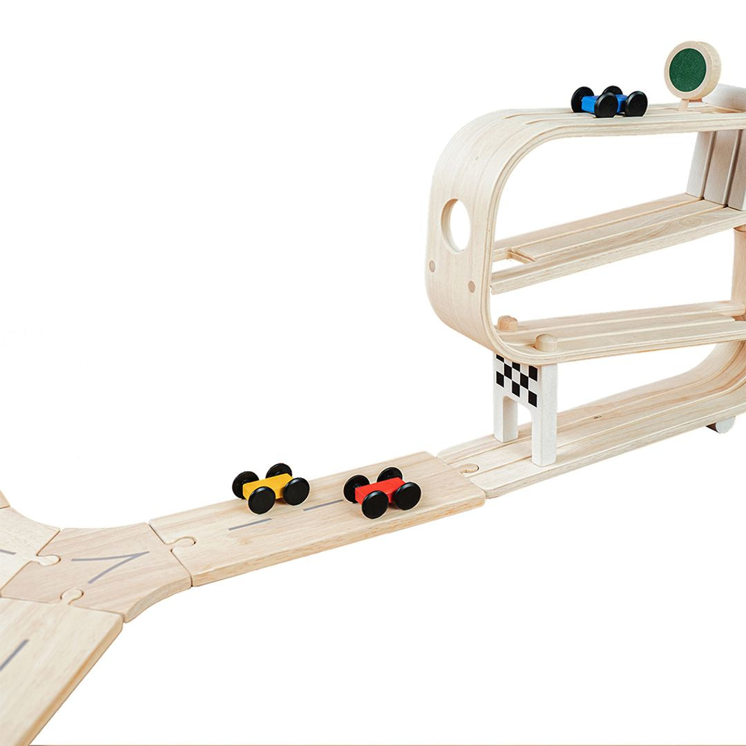 Two toy cars speeding off the PlanToys wooden ramp racer and continuing down the connected road system.