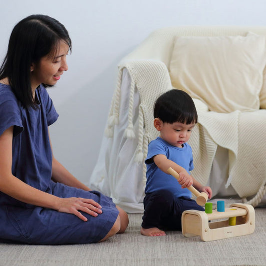 A parent and child playing together with the reversible PlanToys wooden pounding toy on the playroom floor.