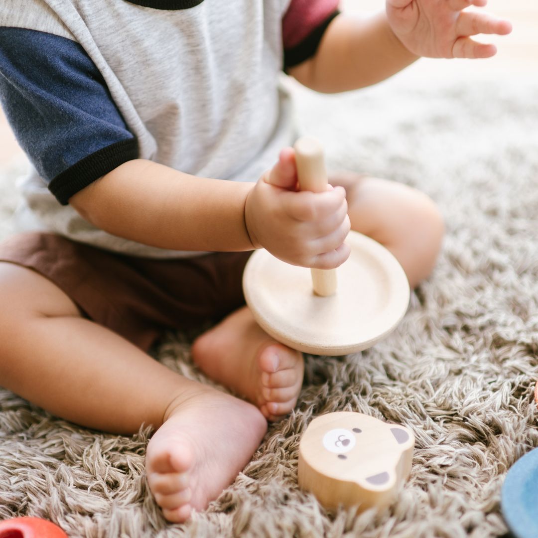 A baby holding the central wooden dowel and base piece of the sustainable PlanToys bear stacking toy.