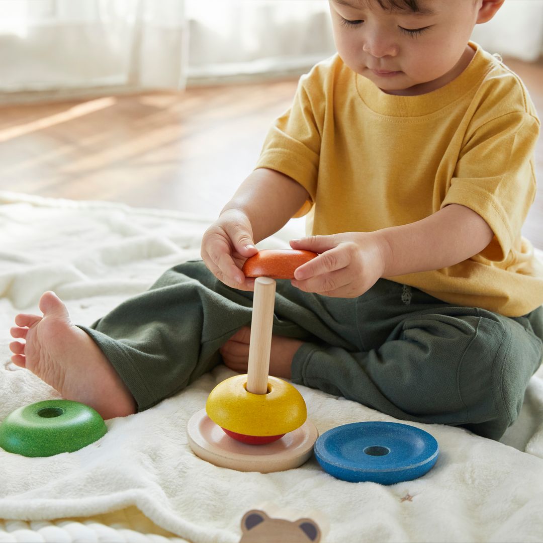 A young child practicing fine motor skills by placing a red ring onto the PlanToys wooden stacker.