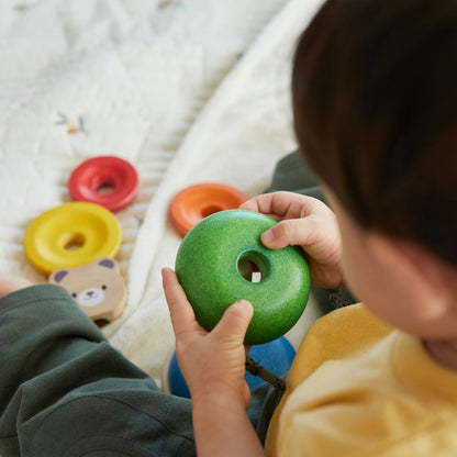 Detailed view of a child's hands holding the green wooden ring from the PlanToys bear stacking set.