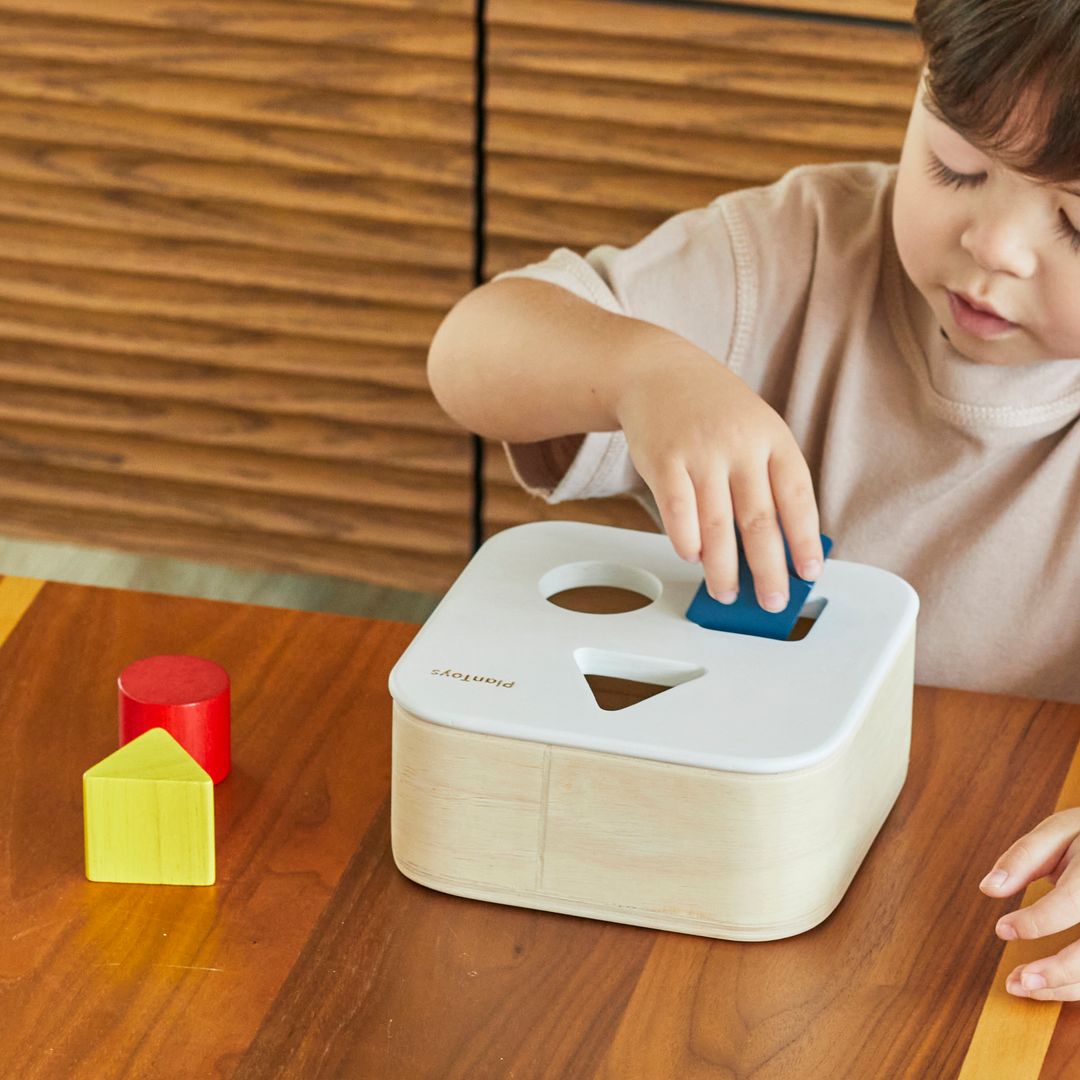A young girl practicing fine motor skills by placing a blue circular block into the sustainable PlanToys shape sorter.