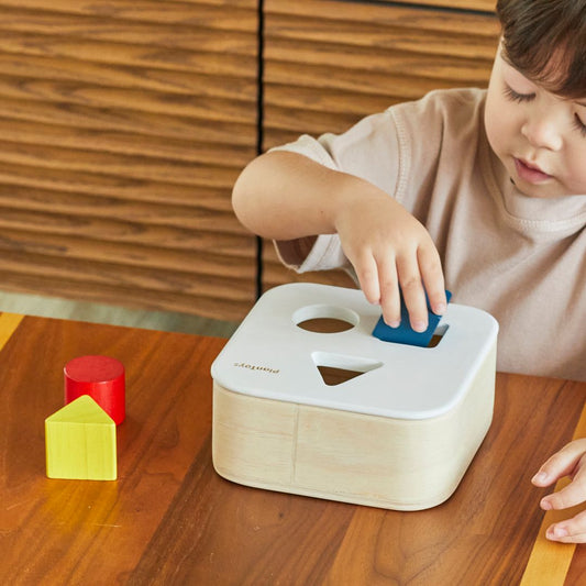 A young girl practicing fine motor skills by placing a blue circular block into the sustainable PlanToys shape sorter.