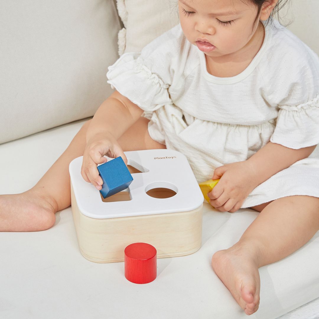 A little girl in a green dress developing hand-eye coordination with the PlanToys sustainable shape sorting bin.