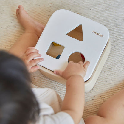 Lifestyle view highlighting the smooth wooden finish of the PlanToys bin during a focused shape-sorting activity.