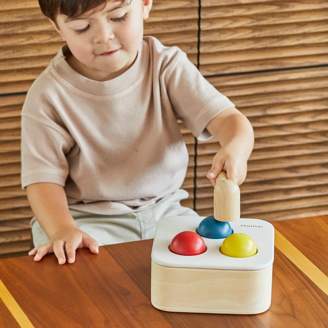 A child's hands holding the wooden mallet to strike the colorful balls on the punch and drop bin.