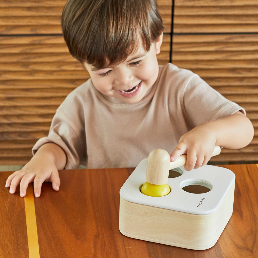 A toddler developing fine motor skills by pushing a wooden ball into the PlanToys hammering toy.