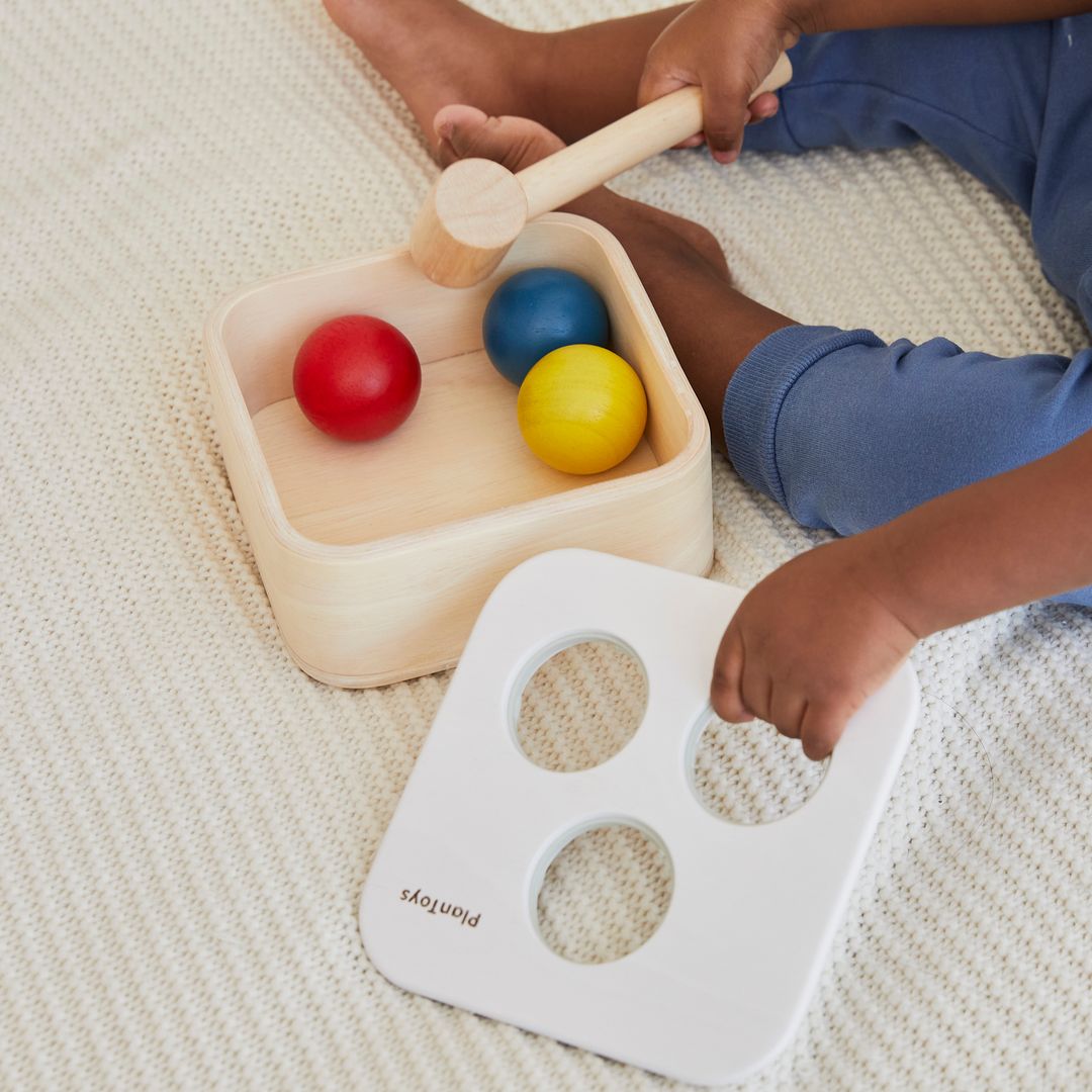 Detailed lifestyle view showing a toddler grasping the mallet for the earth-friendly punch and drop toy.