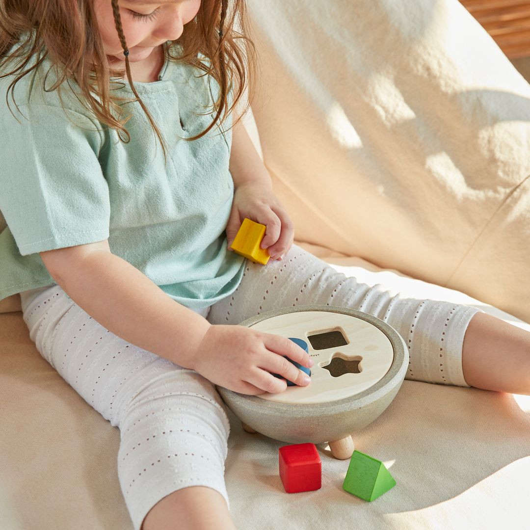 A young child engaged in quiet, focused play with the earth-friendly PlanToys sorting bowl on a soft surface.