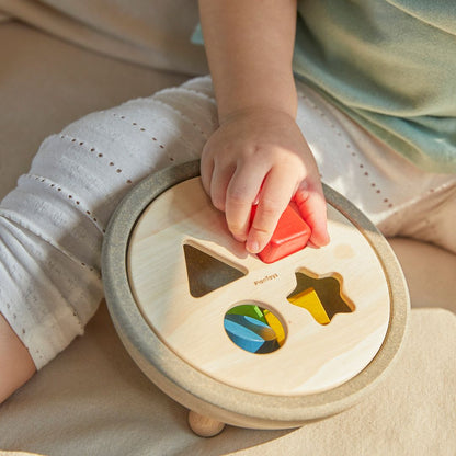 Detailed lifestyle shot of a toddler successfully matching the red square block to the PlanToys wooden shape sorter.