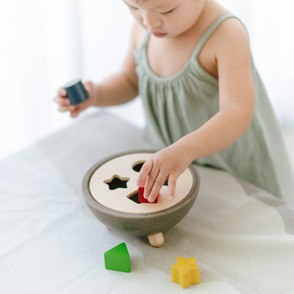 A little girl in a green dress developing hand-eye coordination with the PlanToys sustainable shape sorting bowl.