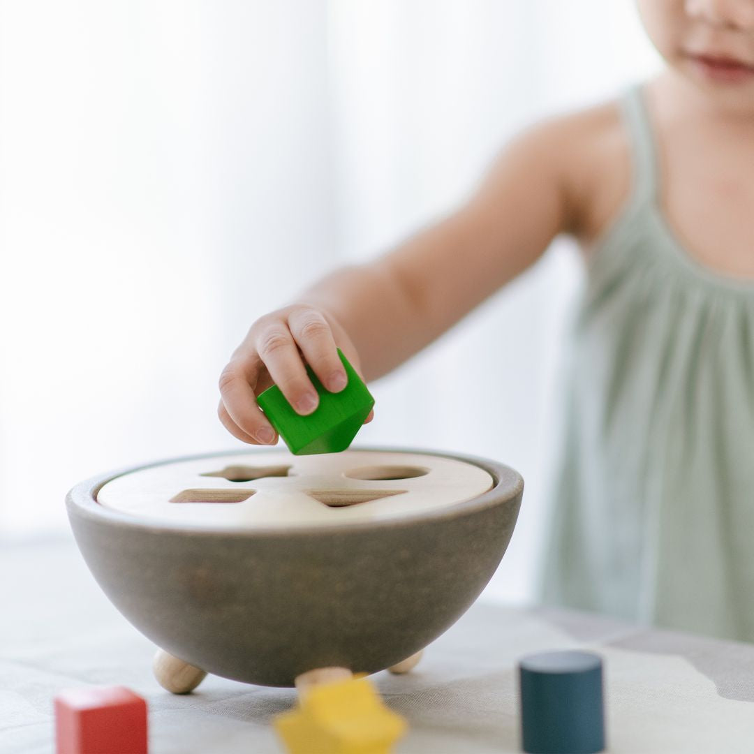 Lifestyle view highlighting the tactile stone-textured PlanWood bowl during a focused shape-sorting activity.