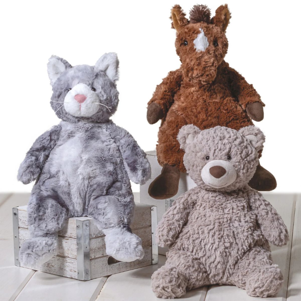 Three Mary Meyer plush toys including a gray cat, brown horse, and beige bear on a light wooden floor.