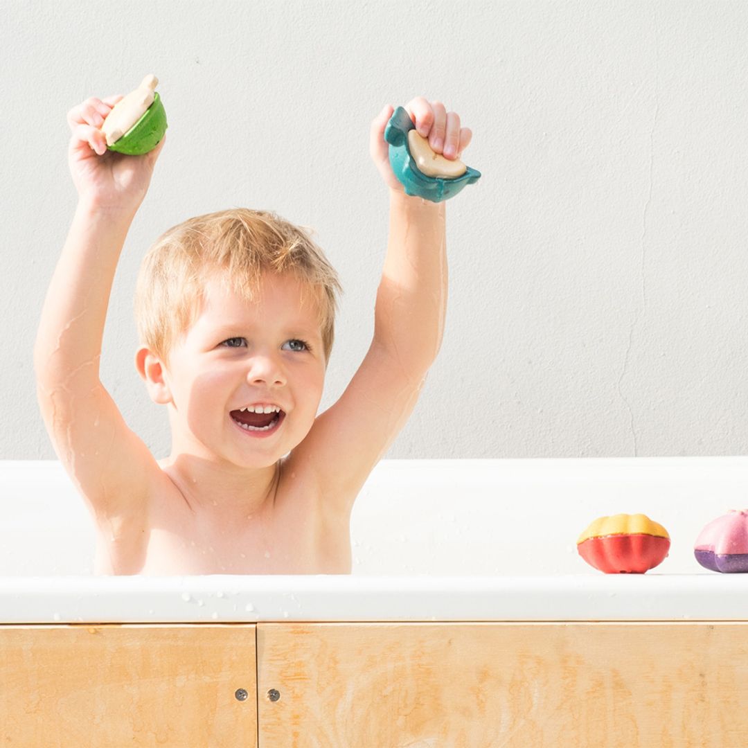 A happy little boy cheering and playing in the bathtub with his non-toxic PlanToys sea life water toys.