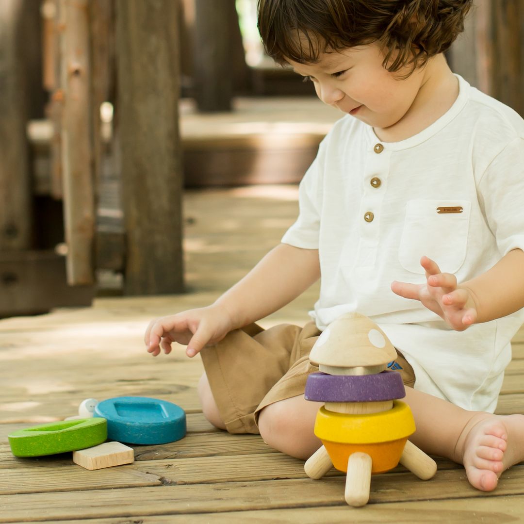 A toddler boy practicing fine motor skills by stacking the wooden rings onto the base of the PlanToys rocket ship toy.