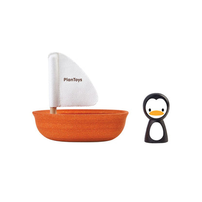 Isolated view of the orange PlanToys sailing boat with white sail next to the separate black and white penguin figure.