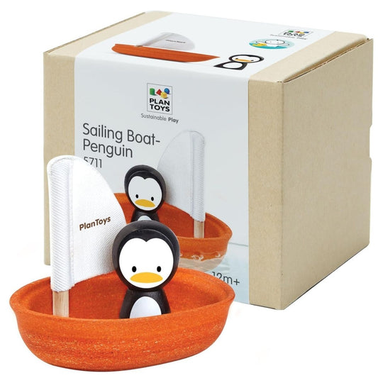 The eco-friendly PlanToys sailing boat and penguin displayed next to its sustainable cardboard packaging.