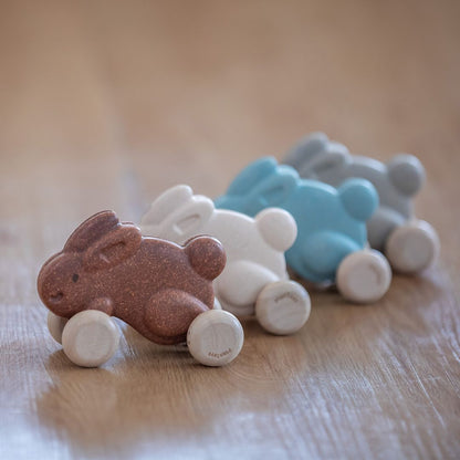A lineup of sustainable PlanToys wooden push along bunnies in brown, white, and blue on a playroom floor.