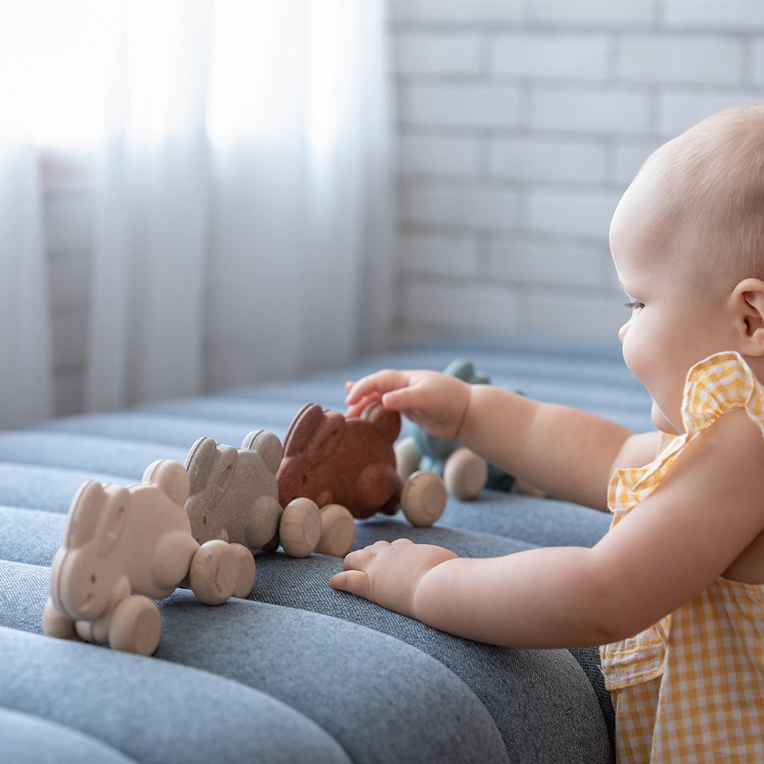A little one practicing fine motor skills by rolling the non-toxic wooden bunny toys across a blue bench.