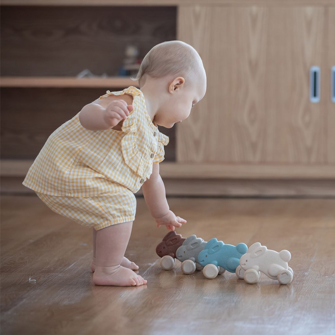 A toddler bending down to push the earth-friendly PlanToys rabbit across a smooth wooden floor, encouraging active play.