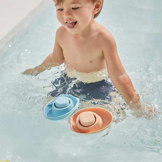 A child enjoying bathtime play with a pastel blue and a peach PlanToys rubber convertible boat.