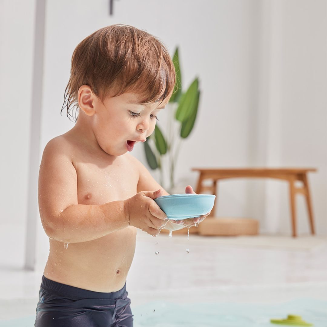 A little boy developing fine motor skills by pouring water out of the hull of the PlanToys rubber boat toy.