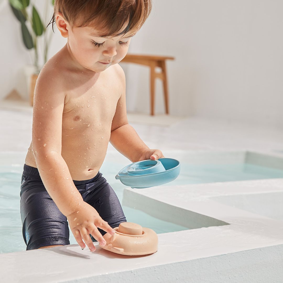 A young boy grabbing his flexible PlanToys rubber boat from the edge of a shallow sensory water pool.