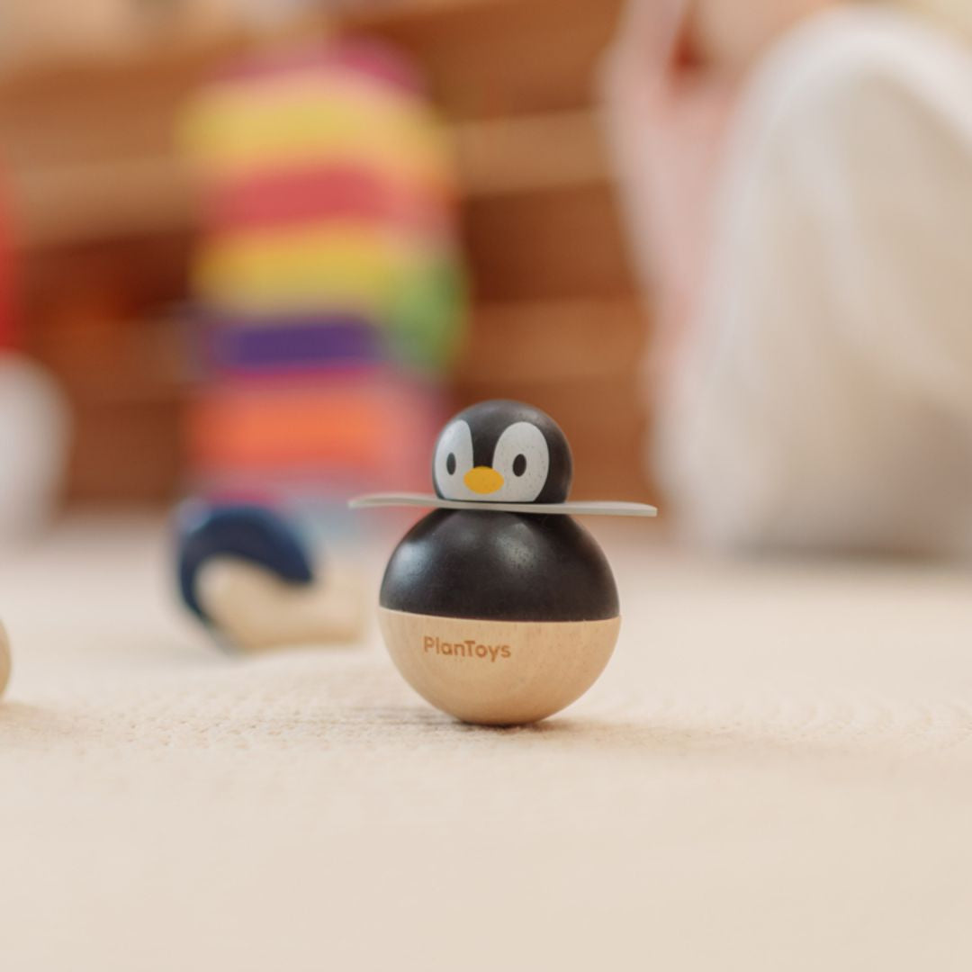The non-toxic PlanToys penguin wobbler spinning and rocking on a playroom floor with toys in the background.