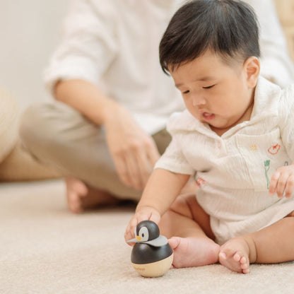 A father watching as his baby practices fine motor skills by reaching for the PlanToys penguin wobbler.