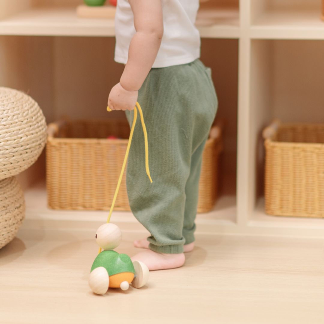A toddler's legs walking across the floor while pulling the sustainable PlanToys wooden duck toy.