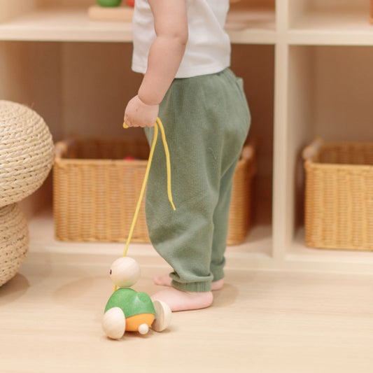 A toddler's legs walking across the floor while pulling the sustainable PlanToys wooden duck toy.