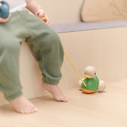A child sitting comfortably on a step while holding the pull cord of their earth-friendly wooden duck toy.