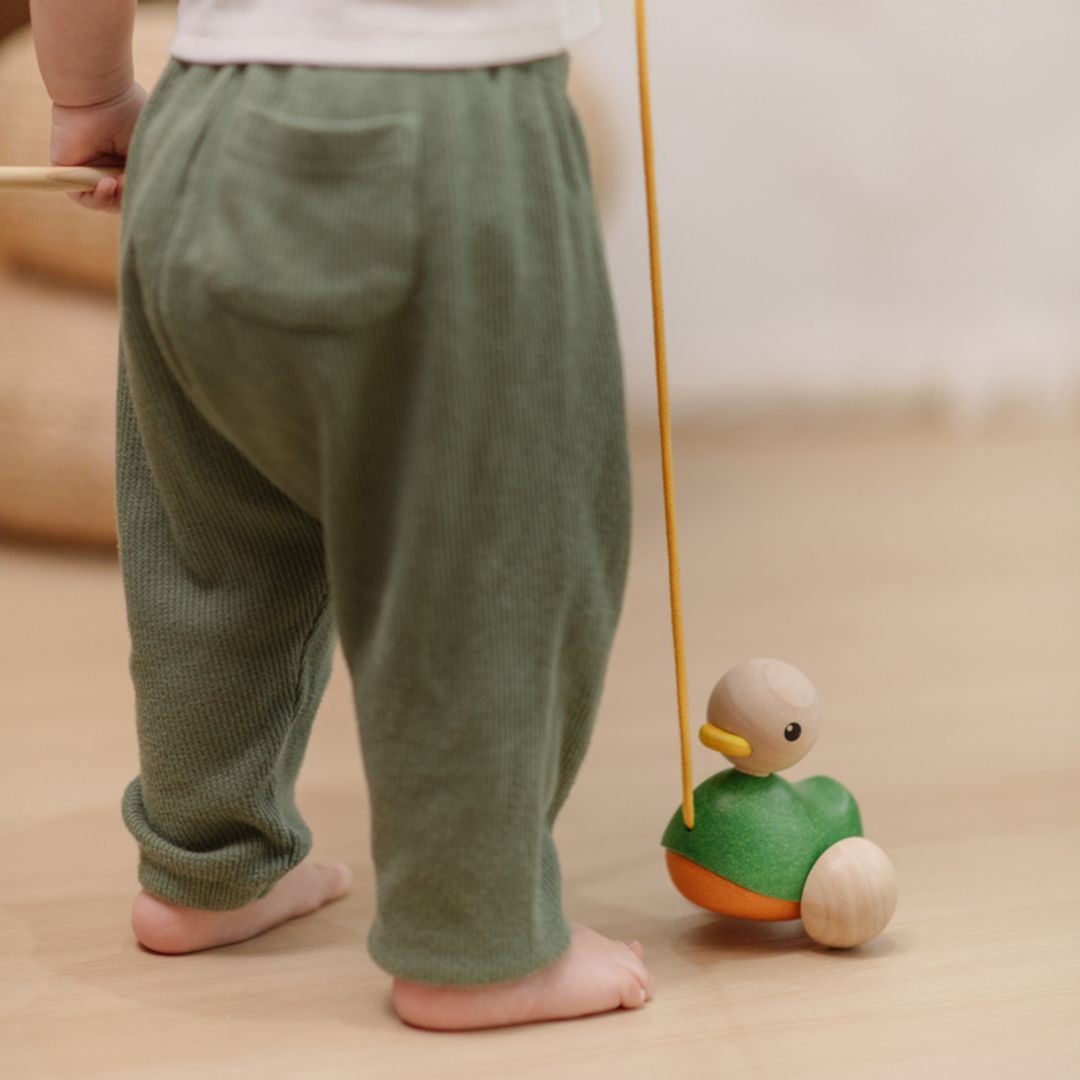 Close-up of a toddler taking steps and towing the durable PlanToys wooden pull toy behind them.