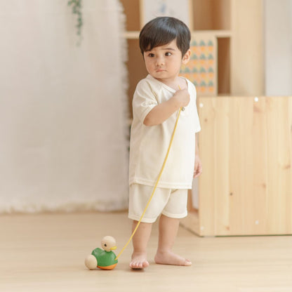 A young boy standing proudly on a wooden floor holding his eco-friendly PlanToys pull along walking toy.