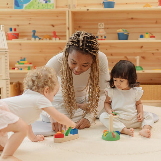 A mother and two toddlers engaging in educational play with the PlanToys shape sorting boat on a playroom floor.