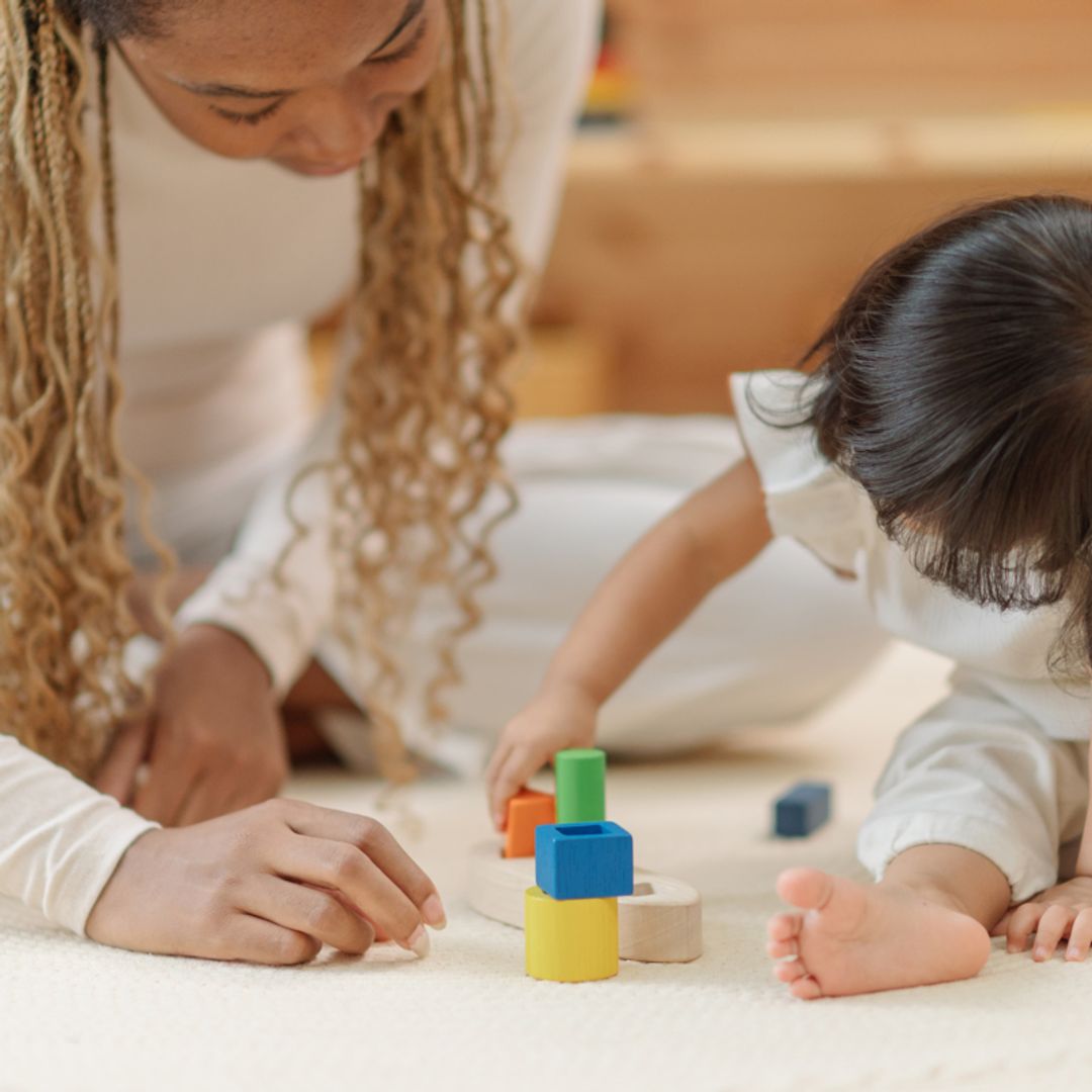 Detailed lifestyle shot of a woman and a toddler girl interacting with the colorful wooden blocks from the PlanToys sorting boat.