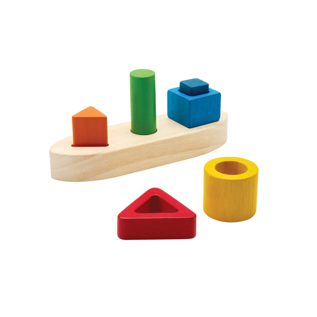 The chemical-free PlanToys wooden shape sorting boat isolated with the red hollow triangle and yellow cylinder resting beside it.